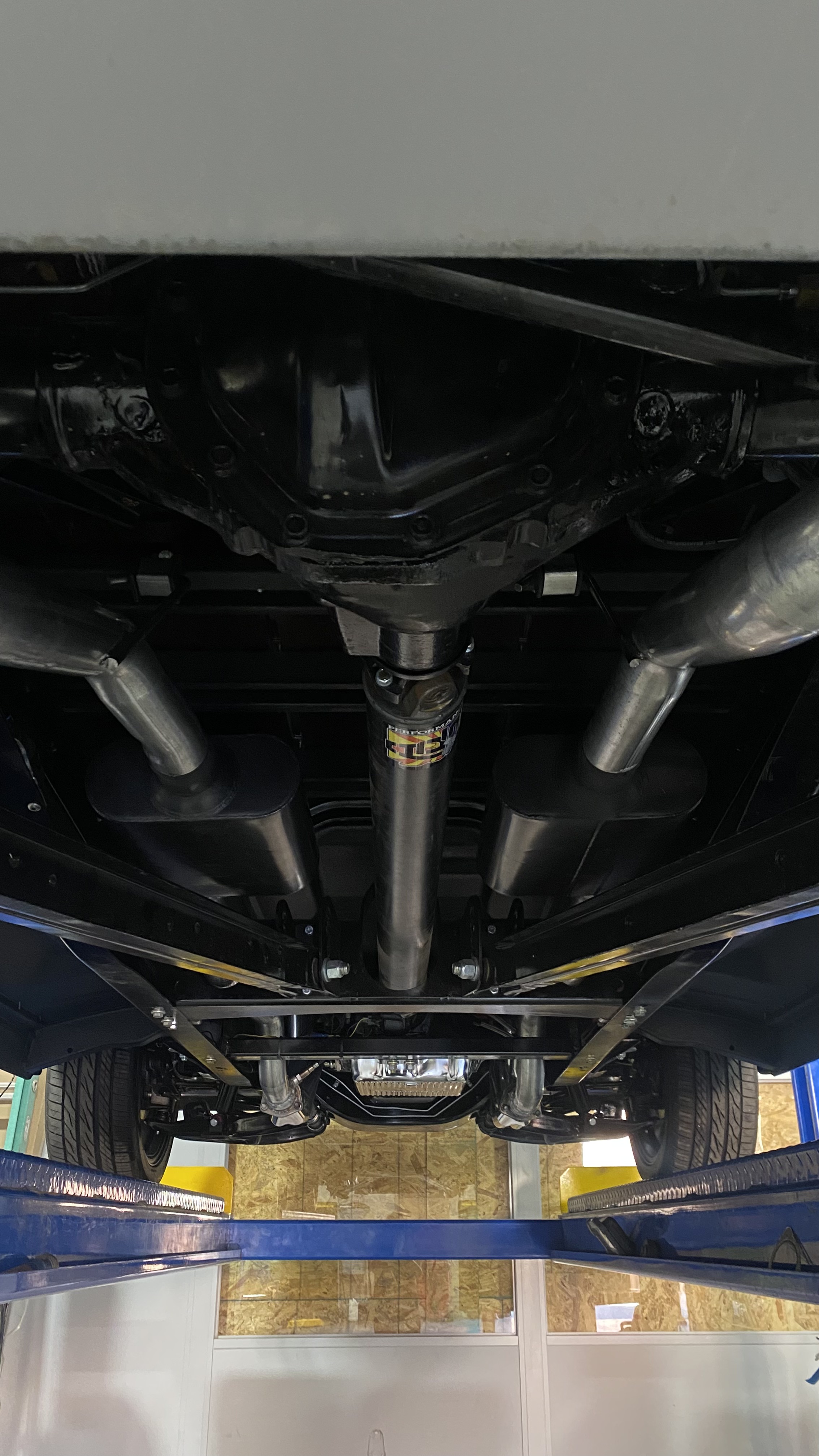 Full dual exhaust system with crossover, twin mufflers, and performance driveshaft, viewed from the rear underbody