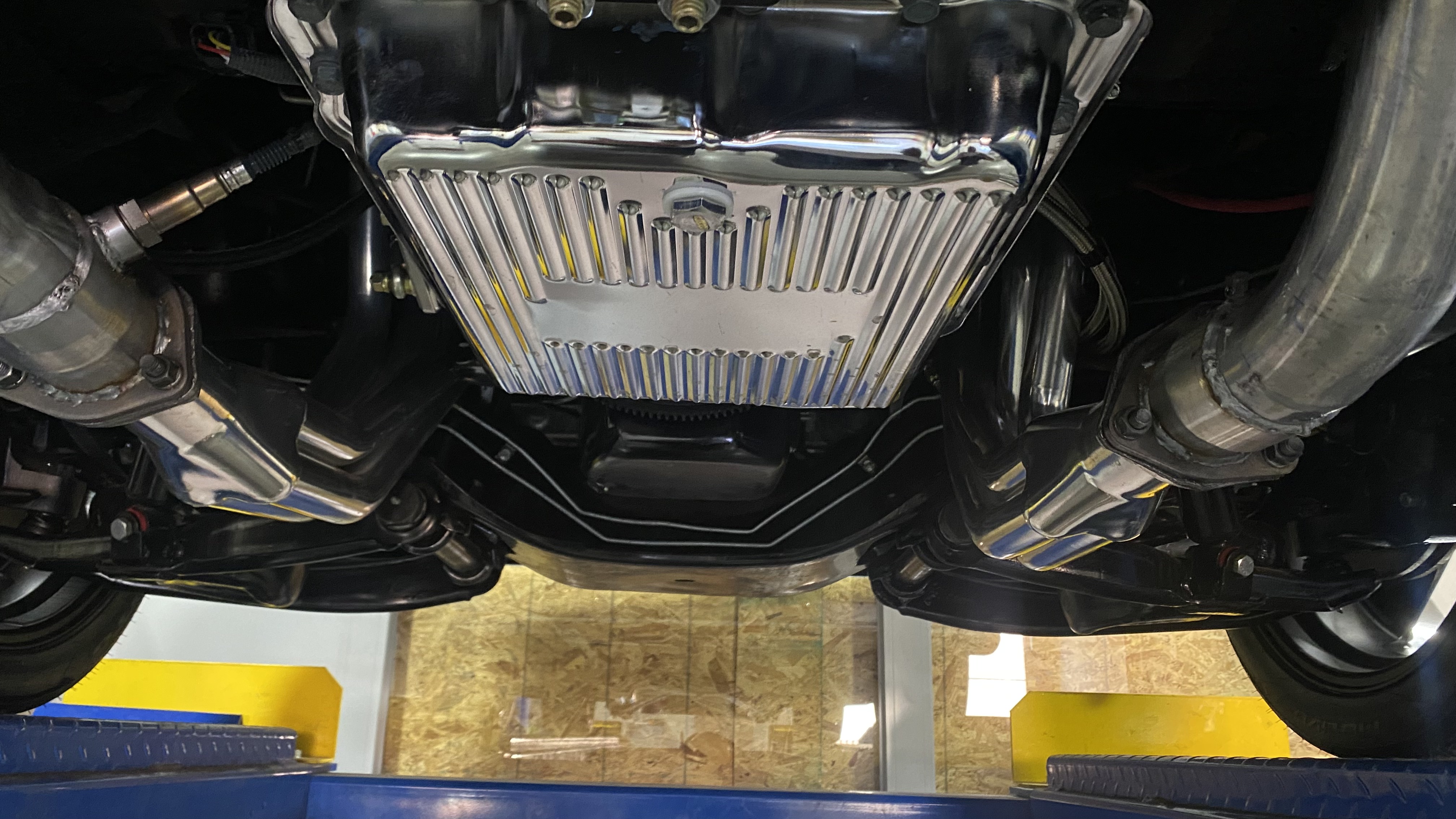 Polished stainless long-tube headers and collectors feeding a custom dual exhaust, viewed from underneath on the lift
